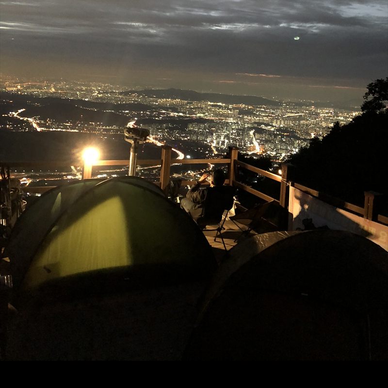 Tents on a mountain terrace at night with city lights spread out below