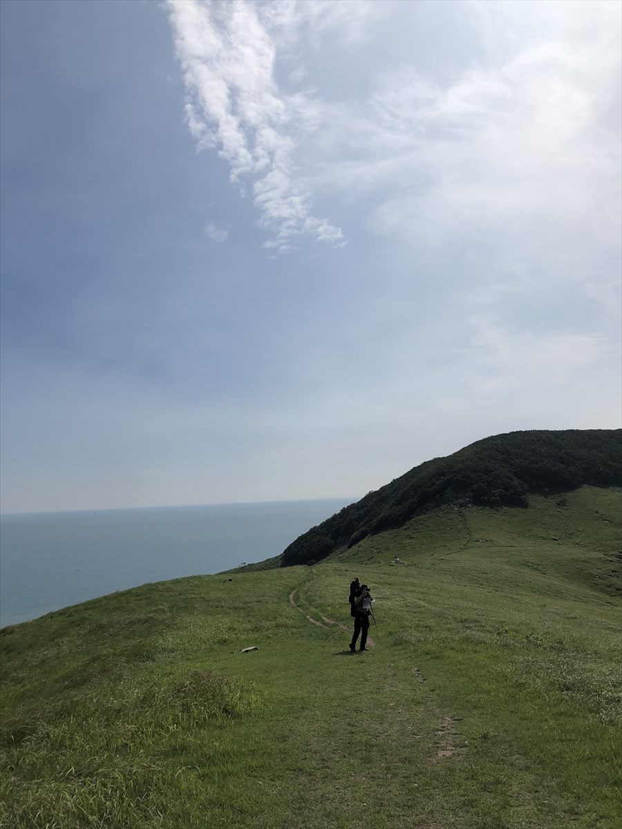 A backpacker walking a grass ridge above the sea on a clear day