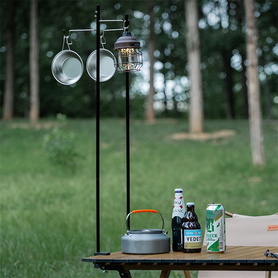 Lantern stand with hanging pans and a kettle beside a camping table in a forest